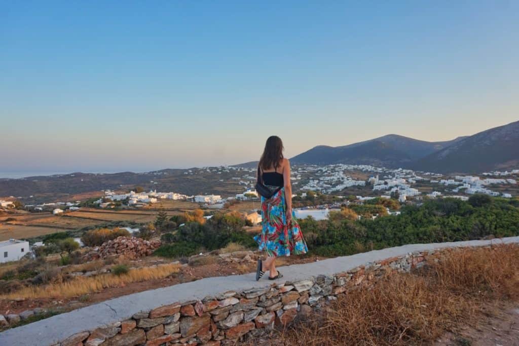 Marie steht auf einer Mauer und blickt auf Sifnos während des Sonnenuntergangs