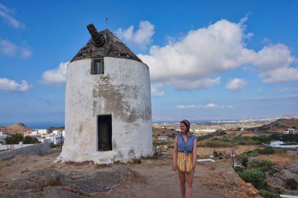 Marie steht vor einer Windmühle in Vivlos mit Blick über die Insel Naxos