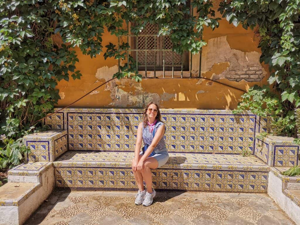 Marie sitzt auf einer gekachelten Bank in den Jardines de Murillo in Sevilla.