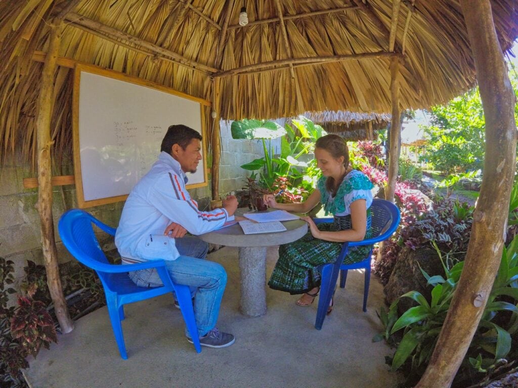 Marie sitzt in einem traditionellen Gewand der Maya beim Spanisch lernen mit ihrem Lehrer in der Community Spanish School in San Pedro La Laguna am Lago de Atitlan im Garten