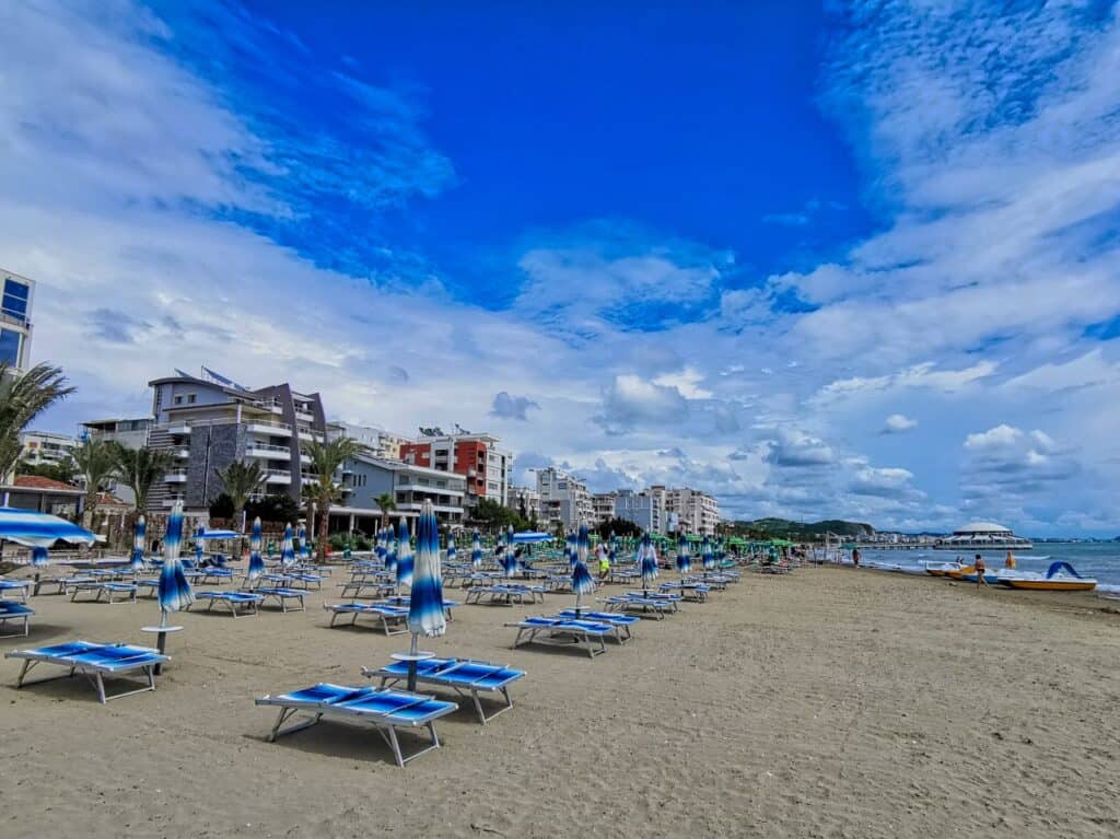 Liegen und Sonnenschirme in blau stehen am Durres Strand in Albanien und im Hintergrund sind Hochhäuser zu sehen