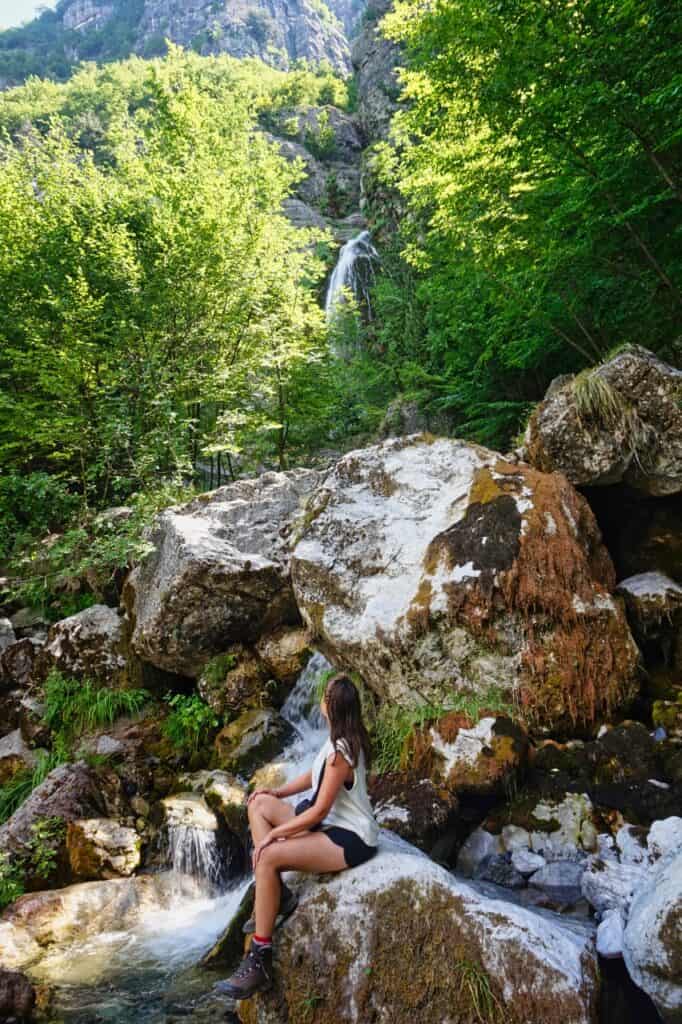 Marie sitzt auf einem Fels am Grunas Wasserfall in den albanischen Alpen.