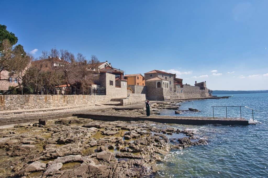 Marie steht am schönen Stadtstrand von Novigrad im Schatten der Stadtmauer.
