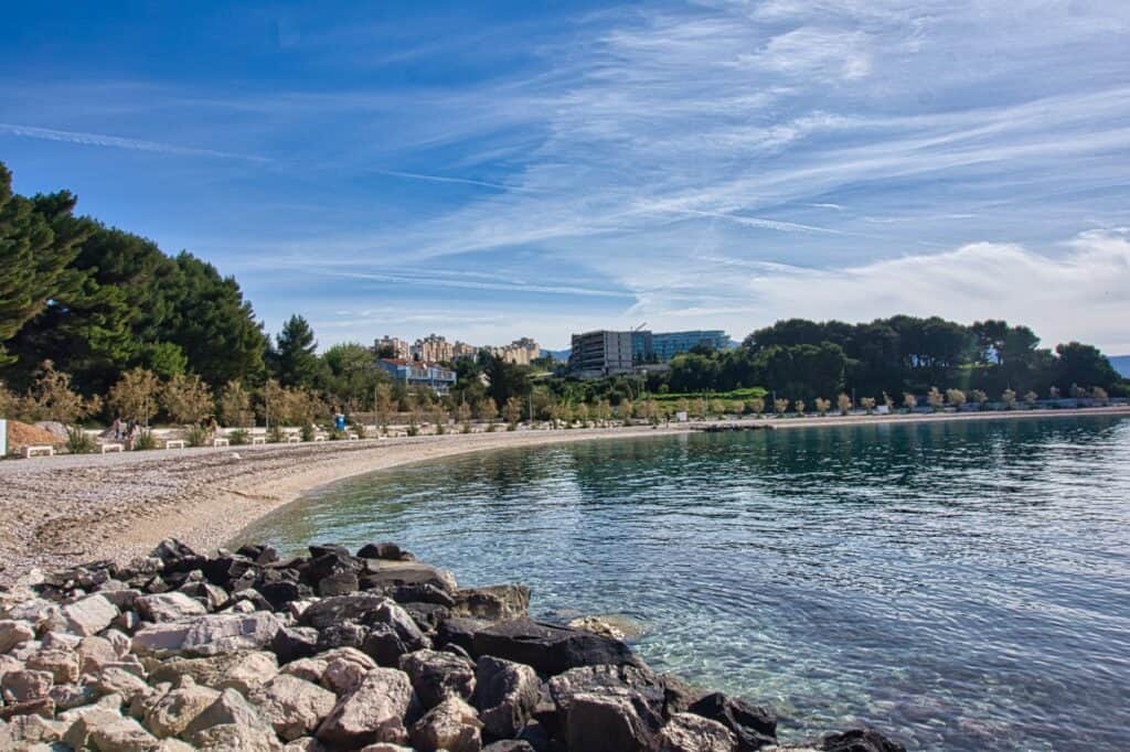 Der Kupaliste Beach in Split mit Felsbrocken im Vordergrund, den schönen Kieselsteinen und Hochäusern im Hintergrund