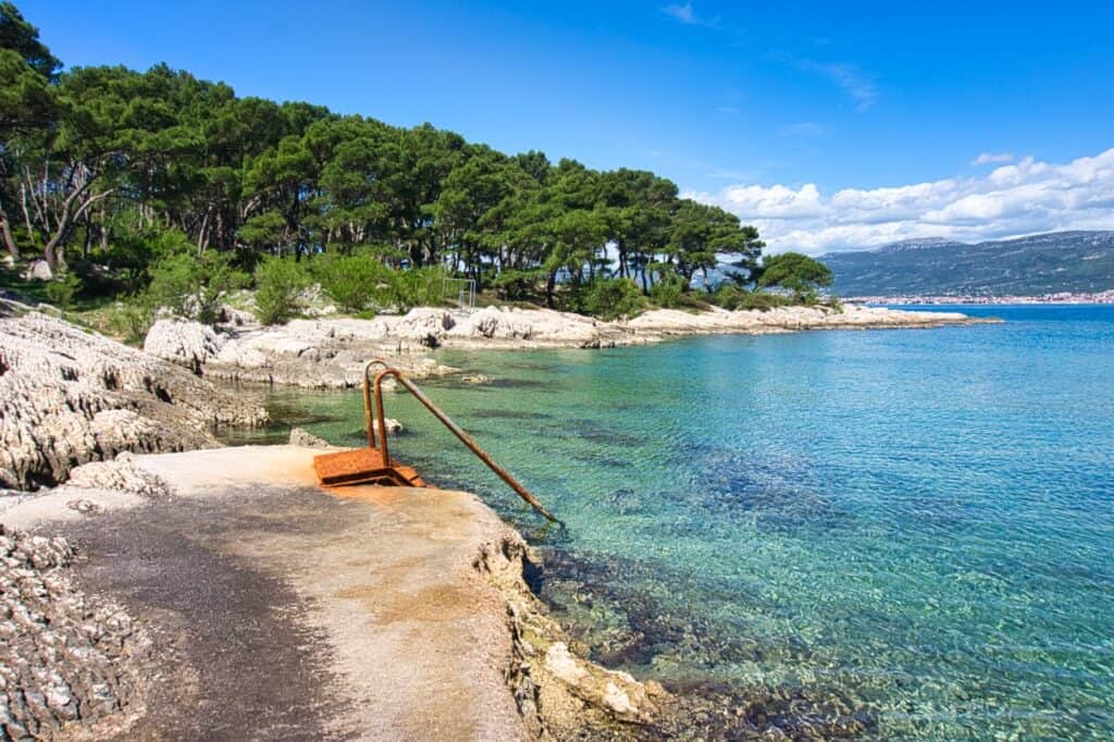 Eine etwas rostige Leiter führt ins kristallklare Wasser am Strand Third Water in Split