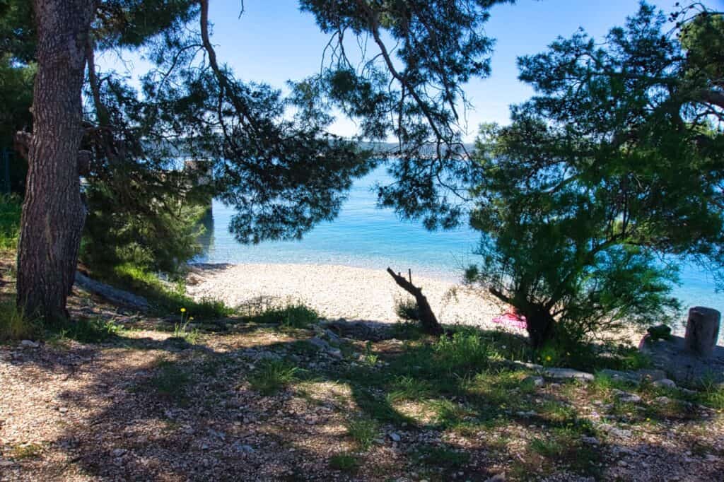 Blick durch die Bäume auf den geheimen Kiesstrand in Split namens Mary's Beach