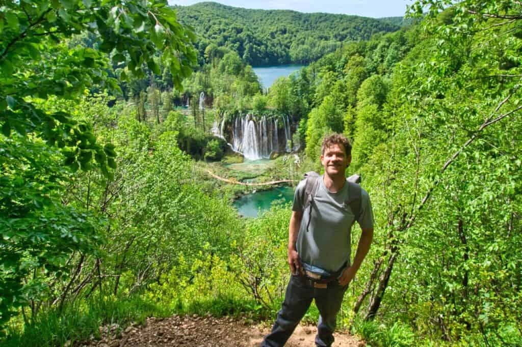 Chris steht vor einem schönen Wasserfall der Plitvicer Seen und muss wegen dem absurd teuren Eintritt fast schon lachen