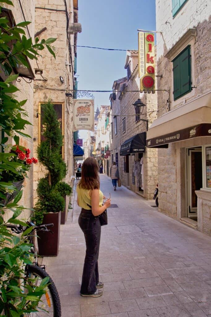 Marie steht in der Hauptgasse von Trogir und schaut sich die schönen Schilder an