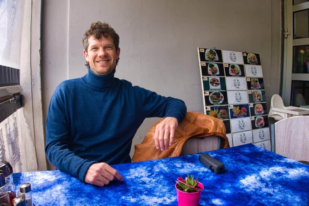Chris sitzt im Restaurant Furia und lacht in die Kamera, neben ihm ist die Speisekarte mit den frischen Tagesgerichten