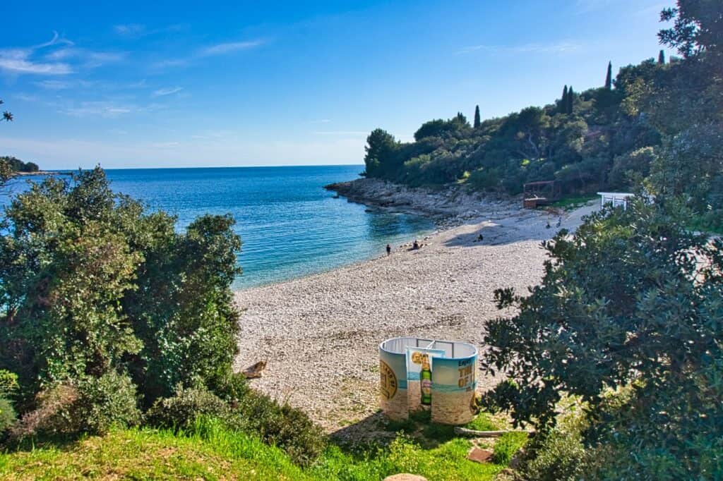 Blick von oben auf den Histria Strand in Pula mit hellem Kies und einer Umkleidekabine