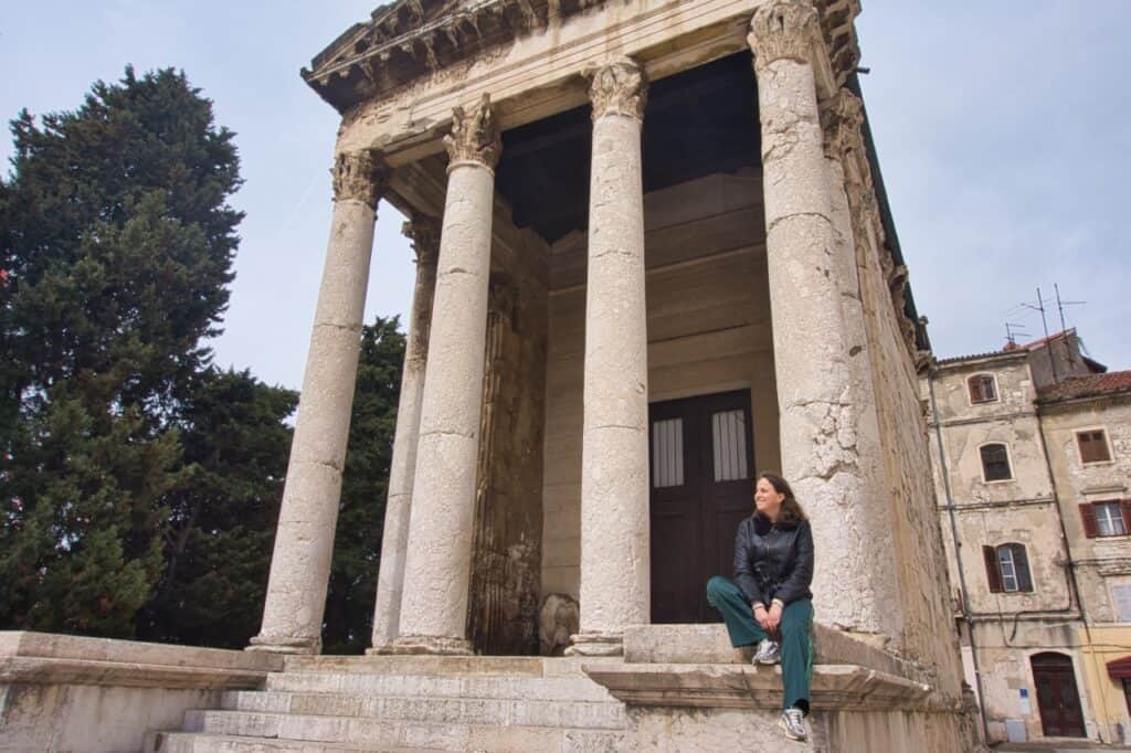 Marie sitzt vor einer der bedeutendsten Sehenswürdigkeiten in Pula, dem Augustustempel und schaut in die Ferne