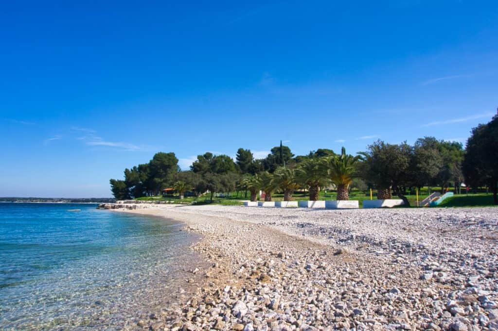 Seitlicher Blick über den Plaza Vile in Pula mit hellem Kies und Palmen im Hintergrund