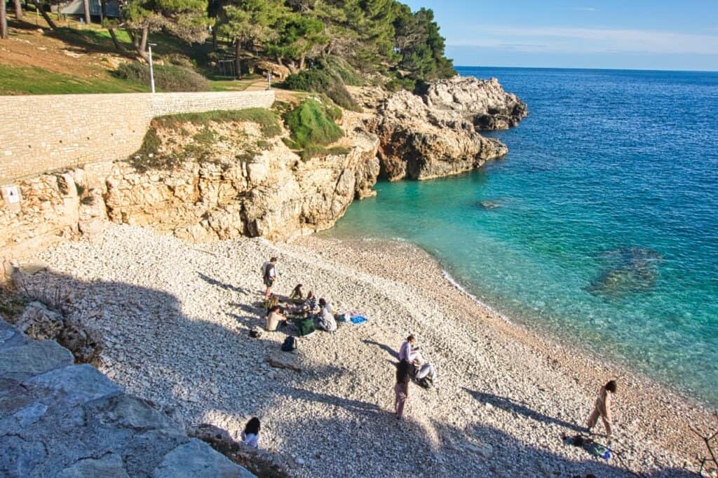 Blick von oben auf den kleinen, aber sehr schönen Hawaii Strand in Pula, an dem einige Menschen liegen